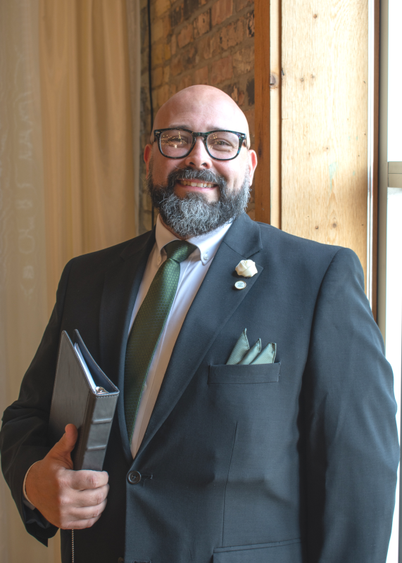 Ashton Bishop is our owner and lead officiant. He is featured here wearing a classic black suit with green tie and pocket square. 